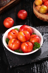 Freshly picked red plums with water droplets in bowl on slate board - healthy organic stone fruit