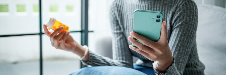 Female Asian holding drug bottle using smartphone for medical details