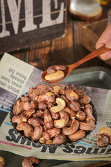 Roasted Cashew Nuts in Wooden Spoon Over Bowl on Newspaper Kitchen Counter
