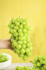 Fresh Green Grapes Bunch in Hand Against Yellow Background - Healthy Organic Fruit