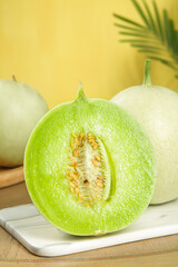 Fresh Jade Green Honeydew Melon Half Cut Showing Seeds on White Board with Tropical Background
