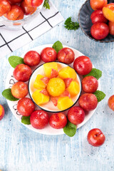 Fresh Red Plums and Yellow Fruit Salad from Guangdong China - March Seasonal Arrangement with Mint on Blue Wood Background