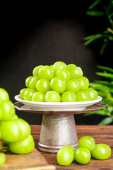 Fresh Green Seedless Grapes on Ceramic Pedestal Plate with Natural Wood Table and Tropical Plants