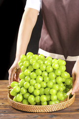 Fresh Green Grapes in Wicker Basket Held by Woman on Wooden Table