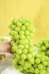 Fresh Green Seedless Grapes Held by Hand on Bright Yellow Background - Healthy Fruit Showcase