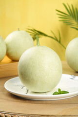 Fresh Jade Melon with Cream Colored Skin on Marble Plate with Mint Leaves and Palm Background