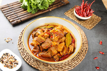 Braised beef cubes in savory sauce with fresh herbs and chili peppers on rustic kitchen table