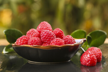 Fresh Red Raspberries in Wooden Bowl with Green Leaves on Natural Background