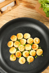 Pan-fried dumplings with herbs cooking in black skillet on wooden kitchen surface