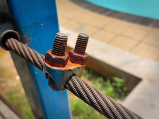 Weathered metal cable secured by two rusty bolts and a clamp against a blurred background.