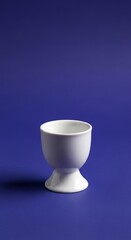 White ceramic egg cup on the deep blue background in studio setting