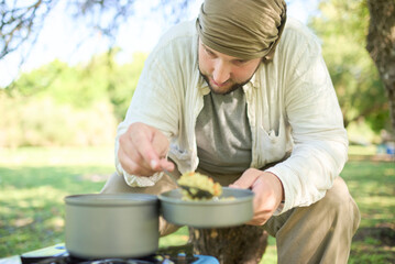 Male traveler serving rice with vegetables he has just cooked on a portable gas stove. Composition with selective focus and copy space.