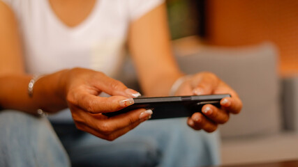 A person sits comfortably on a sofa, focusing on their smartphone in a warm and inviting indoor space, enjoying a leisurely moment of browsing or messaging