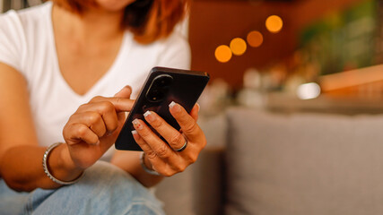 A person is comfortably seated in a cozy cafe, engaging with their smartphone. Warm yellow lights...