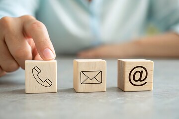 Finger touching wooden blocks with icons of telephone envelope and email for communication and contact methods