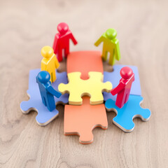 Fototapeta premium Colorful wooden figures represent diverse people connecting on jigsaw pieces. Teamwork, diversity concept visualizes HR strategies for inclusive workplace cultures. Different colored figures connect