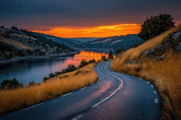 Winding road beside a lake at sunset, fiery sky reflected in still water