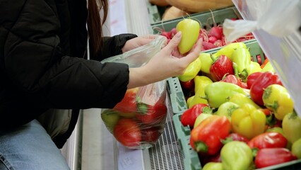 Customer choosing vibrant bell peppers from a grocery store display and packing a plastic bag with fresh produce for a nutritious diet