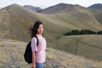 Naklejka premium a teenage girl with loose hair and a black backpack, looking into the camera at the Karamuruntau mountain range