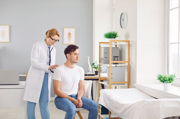 Fototapeta premium Female doctor or nurse using a stethoscope to check the lungs and breathing of a male patient during a hospital checkup. This healthcare visit ensures the patient health and well being.