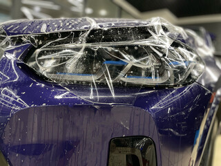A car wrapping specialist applies a polyurethane film on the front headlight of a car. Car...