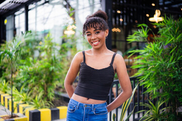 A joyful young woman winks at viewer with a radiant smile, her casual outfit and natural hair...
