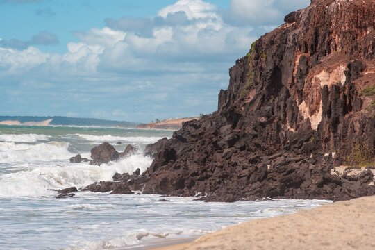 Scenic view of rocky cliffs meeting ocean waves under a partly cloudy sky