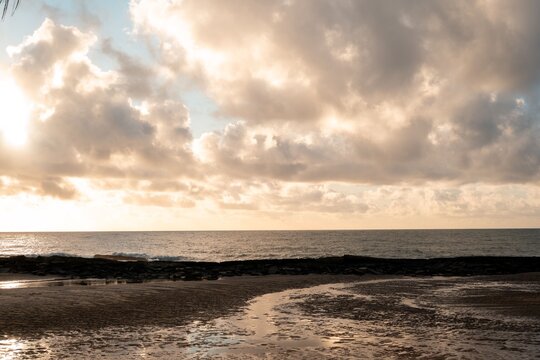 Serene coastal scene with dramatic clouds and sunlight over a tranquil sea at dawn - Powered by Adobe