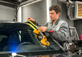 Automobile special workers replacing windscreen or windshield of a car in auto service station garage. Glass of the car, removed with the help of professional suction cups. The process of car repair. 