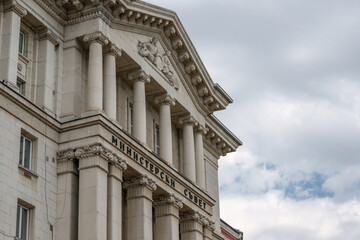 The Council of Ministers building with neoclassical architecture stands beneath heavy clouds, symbolizing political challenges and reflecting its role as a key governmental landmark.