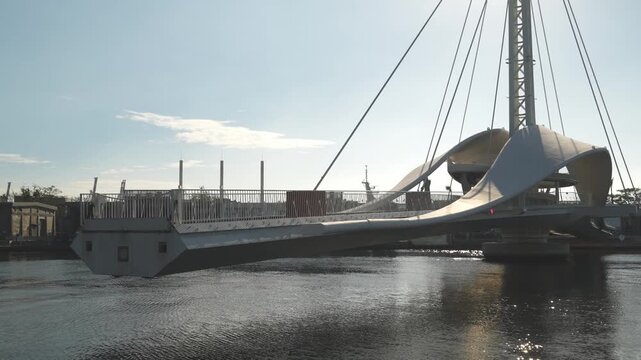 Modern cable-stayed pedestrian bridge spanning a tranquil river under blue sky
