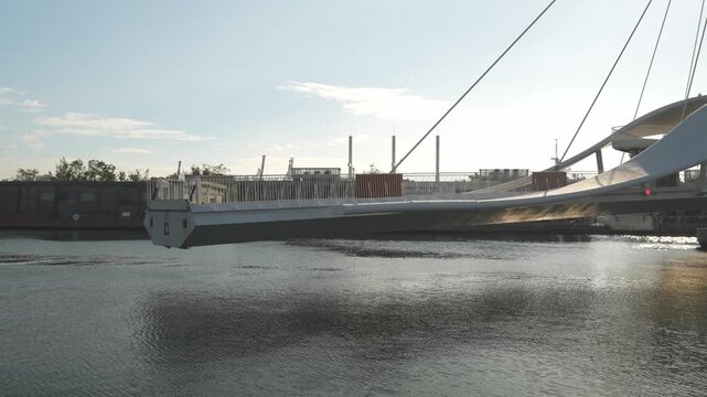 Modern suspension pedestrian bridge over calm urban waterfront at sunset