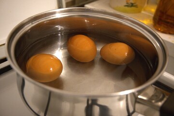 Top view of three brown chicken eggs in water inside a pot, preparation for hard-boiled eggs.