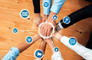 Hands of diverse professionals come together in a modern workspace, symbolizing teamwork,...