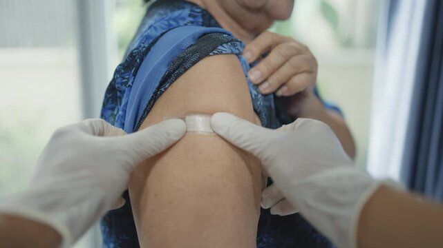 A doctor&rsquo;s gloved hands are applying a bandage after vaccinating a senior woman,Close-up