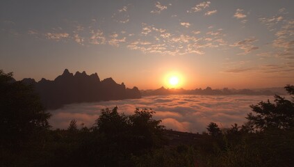 Fototapeta premium Scenic sunrise over a sea of fog, with mountainous peaks silhouetted in the distance. Warm light filters through the clouds