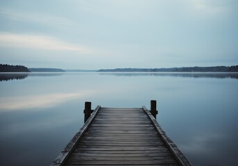 Fototapeta premium Rustic Wooden Pier Leading into Still, Reflective Lake Water Under a Grey Sky