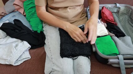 A person organizes and folds various items of clothing efficiently into a suitcase. The high level of packing demonstrates space-saving techniques while preparing for travel