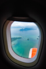 Aerial view from airplane window showing tropical islands, turquoise sea, and clouds with aircraft engine