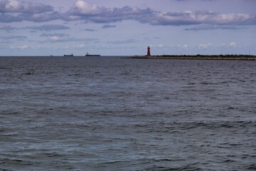 Calm waters and a distant lighthouse guide ships near a coastal harbor during late afternoon