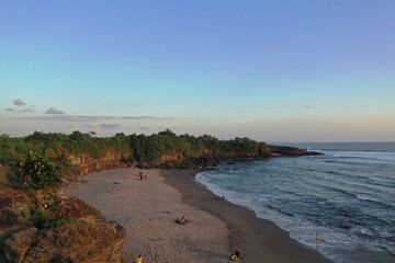 Aerial drone photo of a tropical ocean coastline with a wide sandy beach illuminated by warm golden sunset light