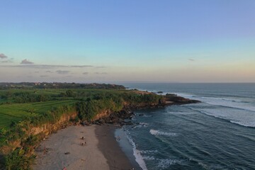 Aerial drone photo of a tropical ocean coastline with a wide sandy beach illuminated by warm golden sunset light