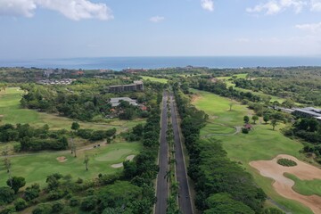 Obraz premium Drone aerial photo of a wide straight tropical road lined with palm trees, with golf courses stretching on both sides