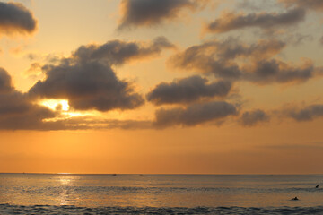 Ocean panorama with cloudy orange sky and setting sun through the clouds