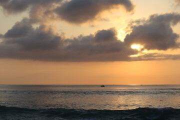Ocean panorama with cloudy orange sky and setting sun through the clouds