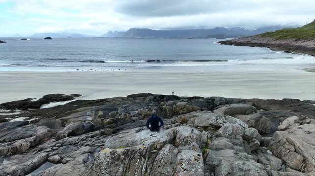 Aerial parallax of photographer on Rorvik Beach with camera set up for timelapse in Lofoten, Norway, Nordland County.