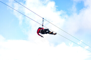 A person soars through the air on a zipline, against a backdrop of blue sky and fluffy white clouds.
