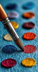 Close-up of paintbrush touching colorful paint dots on textured surface