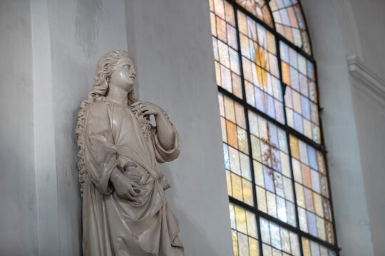 White marble religious figure statue with colorful stained glass window backdrop
