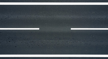 Fototapeta premium Aerial view of a dark asphalt road with clear white lane markings indicating traffic direction and separation on a bright day